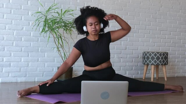 After doing the exercise with outstretched arms to the foot of the leg, the black woman slowly lifted part of the body and took a straight position Yoga at home via the Internet with an online trainer