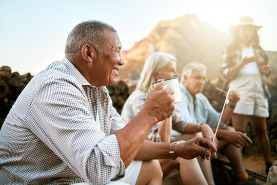 . Relaxed senior camping with friends, taking a break and drinking a cup of coffee while enjoying retirement keeping healthy outdoors in nature. Smiling retired man on a getaway wellness retreat.