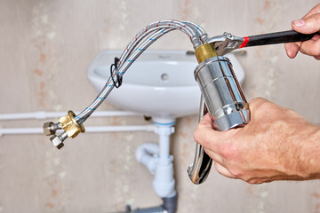 Plumber fixes connecting hoses on water faucet before installing faucet on bathroom sink.