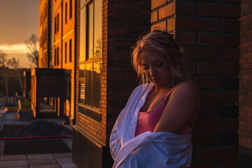 The dark portrait of a young woman with makeup at sunset against the background of a brick wall