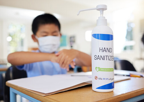Boy rubbing hand sanitizer for hygiene, safety and protection against covid at school. Closeup bottle of alcohol gel on desk in classroom to clean, kill or prevent the spread of germs or coronavirus - Powered by Adobe