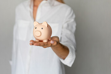 female hands puts a coin in a pink piggy bank. The concept of saving money or savings, investment