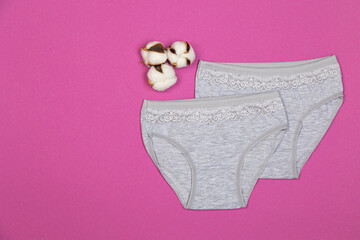 Clothes for children in the form of panties on a pink background. Clothes for children from soft fabric. Panties for girls and cotton flower top view flat lay with copy space for text.