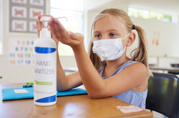 Little student sanitizing hand to protect from covid, wearing a mask and following new hygiene safety routine. Kindergarten or preschool female learner protecting herself from corona virus flu