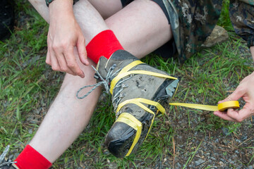 torn, worn trekking hiking boots with a torn sole on the feet of a person, a tourist, on which he wrapped an insulating tape in a hike in nature