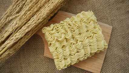 Crispy and dry instant square noodle. Uncook and unhealthy dried noodle on cutting board with dry wheat . asian ramen instant noodles isolated on on burlap surface.