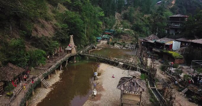 Aerial view of Cat Cat village in Sapa. A traditional tourist village with rickety bridges and walkways over a brown river. 