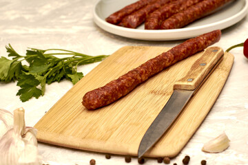spicy smoked sausages on a cutting board next to red pepper garlic spices and herbs on the table