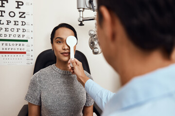Eye exam, vision testing at an optometrist with young woman and doctor. Opthamologist using an occluder to test eyesight before being fitted with glasses. Relaxed lady smiling, satisfied with service