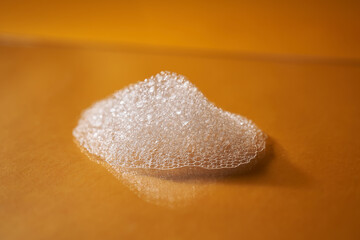 White foam from shampoo or shower gel on a bright yellow background.
