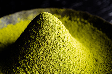 Japanese traditional green tea (matcha) powder in a heap on a black round plate against a black...
