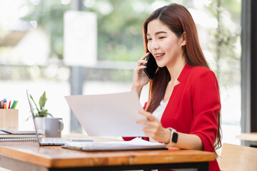 Young Business Asian woman talking on a smartphone and working in an office. Asian female Business accountant Documents data sitting at his workplace.