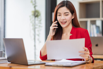 Young Business Asian woman talking on a smartphone and working in an office. Asian female Business accountant Documents data sitting at his workplace.