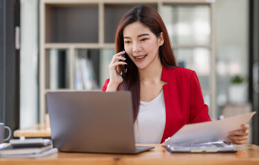 Young Business Asian woman talking on a smartphone and working in an office. Asian female Business accountant Documents data sitting at his workplace.