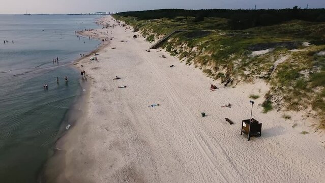 Cinematic Drone shot of people in the beach by the Baltic sea. Amazingly long beach with white sand and  green, blue water.