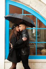 The loving couple in the rain - Beautiful girl holding an umbrella while her boyfriend hugs her in the rain - She looks at him with sincere love