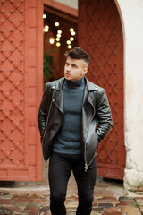 Stylish guy with a fashionable hairstyle in a leather jacket posing on the street.