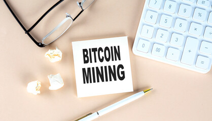 BITCOIN MINING text on sticky with pen ,calculator and glasses on a beige background