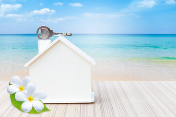 Wooden house model with house key over beach background, summer house, peroperty and real estate business concept