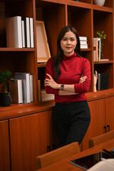 Successful Asian businesswoman stands with her arms crossed in her classic luxury private office.