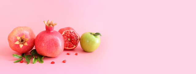 Rosh hashanah (jewish New Year holiday) concept. Pomegranate and apple traditional symbols over pink background