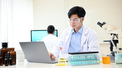 Intelligent and handsome young Asian male scientist working in his office, using laptop.