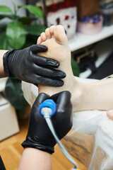 A manicure and pedicure master grinds a foot in a pedicure salon. Black gloves on his hands. Foot...