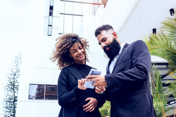 business couple outside corporate building. caucasian man with long beard showing his female partner something on his mobile having fun outdoors