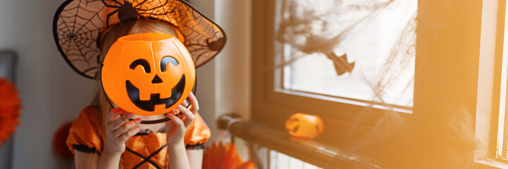 Little Girl in costume of which in decorated bedroom at home. Happy Halloween concept - obrazy, fototapety, plakaty