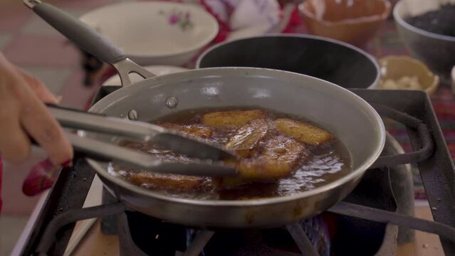 Indigenous woman flips plantains cooking in a pan of oil. 