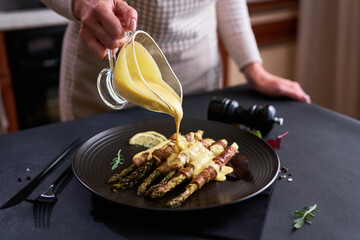 baked aspargus covered with bacon on a black ceramic plate