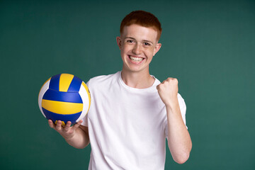 Successful red head boy holding volleyball ball and looking at camera