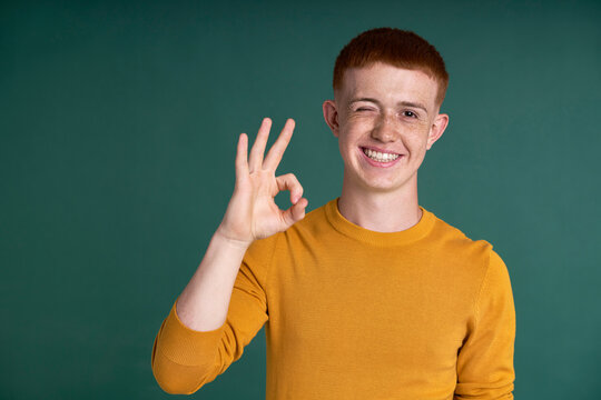 Smiling caucasian male teenager showing perfection sign made with hands