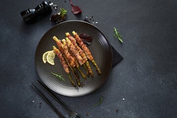 baked aspargus covered with bacon on a black ceramic plate