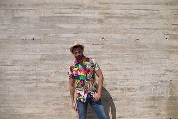 Handsome young man wearing a shirt with Hawaiian flowers, a hat and a necklace with coloured...