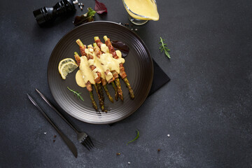 baked aspargus covered with bacon on a black ceramic plate