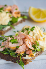 Smorrebrods, open Danish sandwiches with baked salmon, egg salad and microgreens on a white ceramic board against a light concrete background. Sandwich recipes.