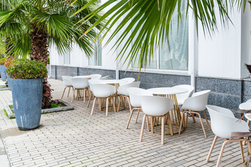 Street cafe with white chairs, green foliage around. Without people, tourism, travel.