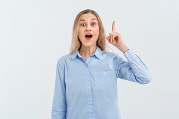 Surprised and amazed blonde girl gestures with hand, pointing finger up to show best deal, showing advertisement. Indoor studio shot on white background