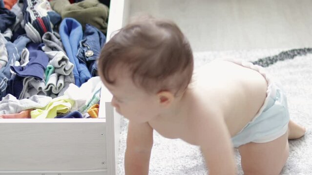 cute baby boy playing on the floor gray carpet taking out the clothes from drawer or get up, crawling around.toddler wear washable cloth diaper,eco alternative.morning situation,maternity concept
