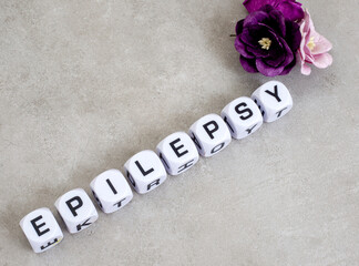 Epilepsy written in dice with paper flowers on mottled grey with copy space