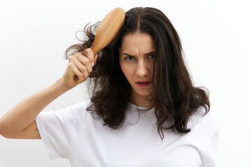 Fototapeta premium a sad, upset woman tries to comb her long, dark, tangled hair with a wooden massage comb. Hair care topics