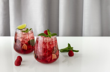Fresh summer lemonade with raspberry, lime, soda water, and ice in glasses. Cold refreshing drink, cocktail or mocktail.