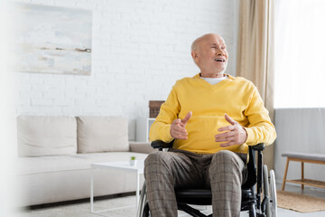 Fototapeta premium Positive elderly man looking away while sitting in wheelchair at home.