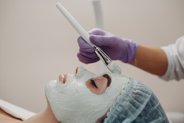 Young woman applying mask of clay on face in beauty spa.
