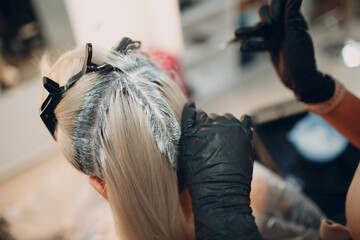 Young woman hairdresser dying hair at beauty salon. Professional hair roots coloring.