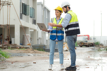 Engineer man and female architect wear safety helmets discuss housing development project at...