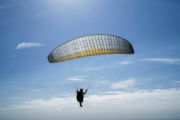 Closeup of a person Paragliding under the blue cloudy sky on a sunny day