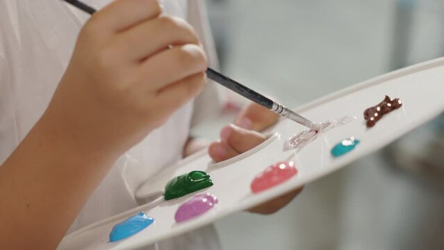 Little girls hand mixes paints with brush on palette. Extrime close up view, Acrylic Painting