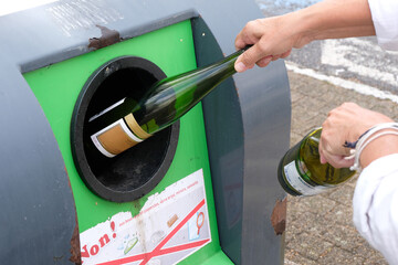 Quelqu'un déposant des bouteilles en verre vides dans un conteneur de recyclage en gros plan